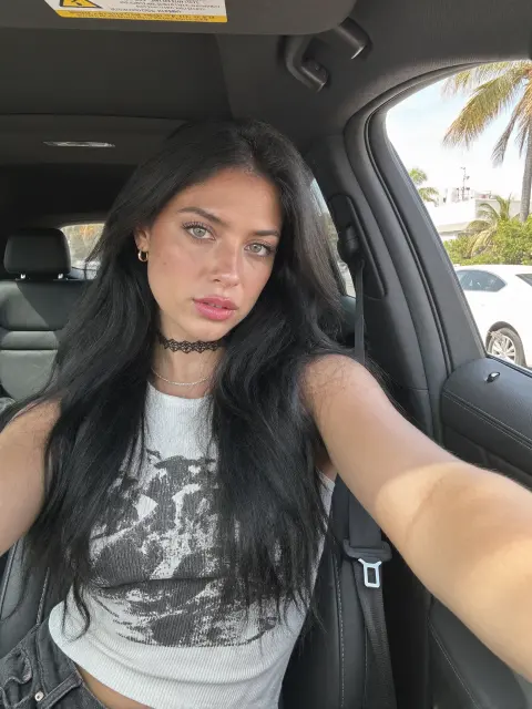 AI photo of a woman with long thick black wavy hair: car selfie in a graphic tank, made with KREA 2