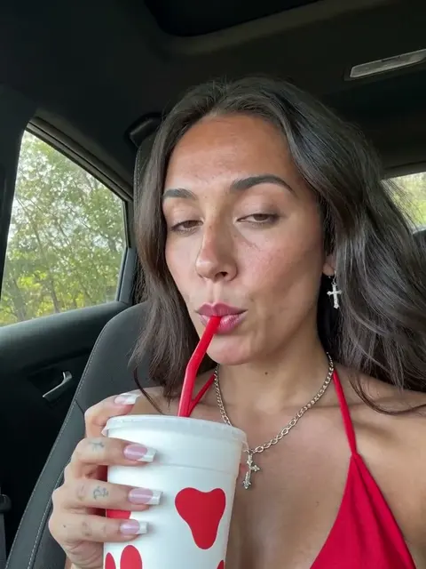 Frame from an AI video of a woman with long dark wavy hair: car talking video with an iced drink, made with MiniMax H3