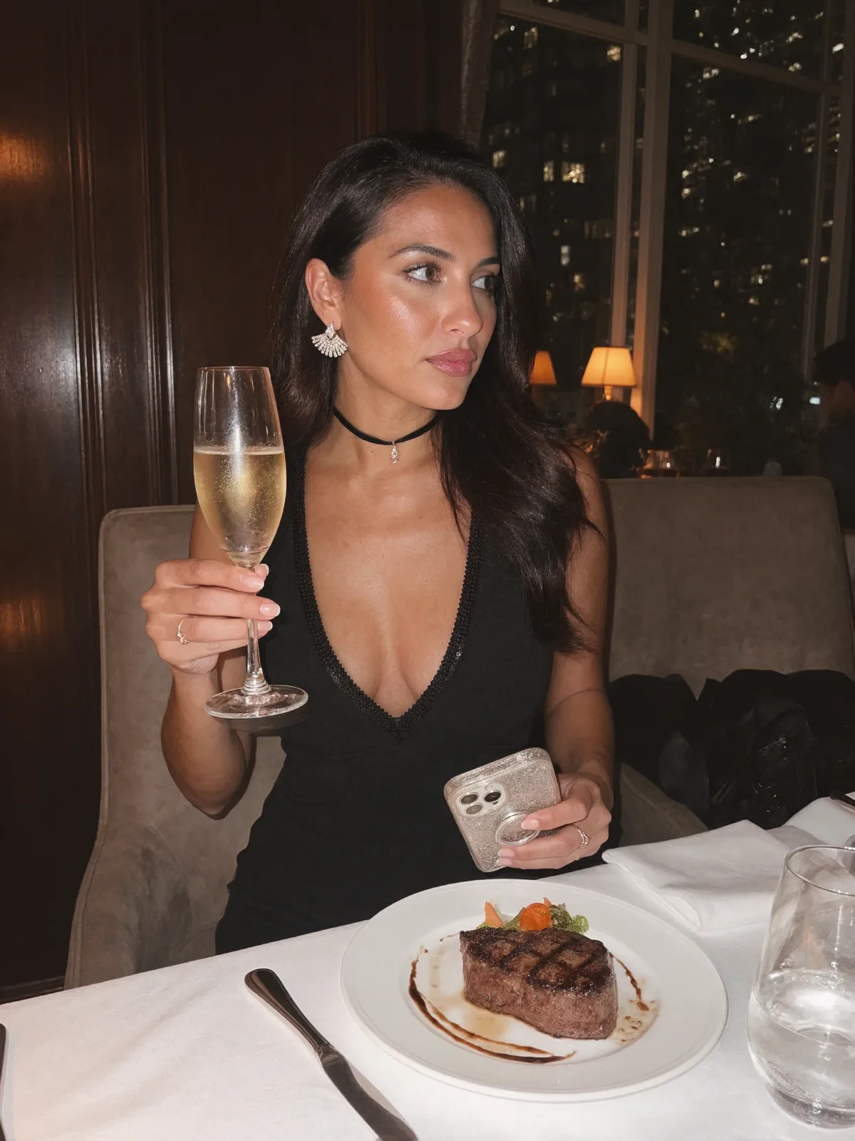 AI photo of a woman with long dark wavy hair: champagne and steak dinner in a black dress, made with KREA 2
