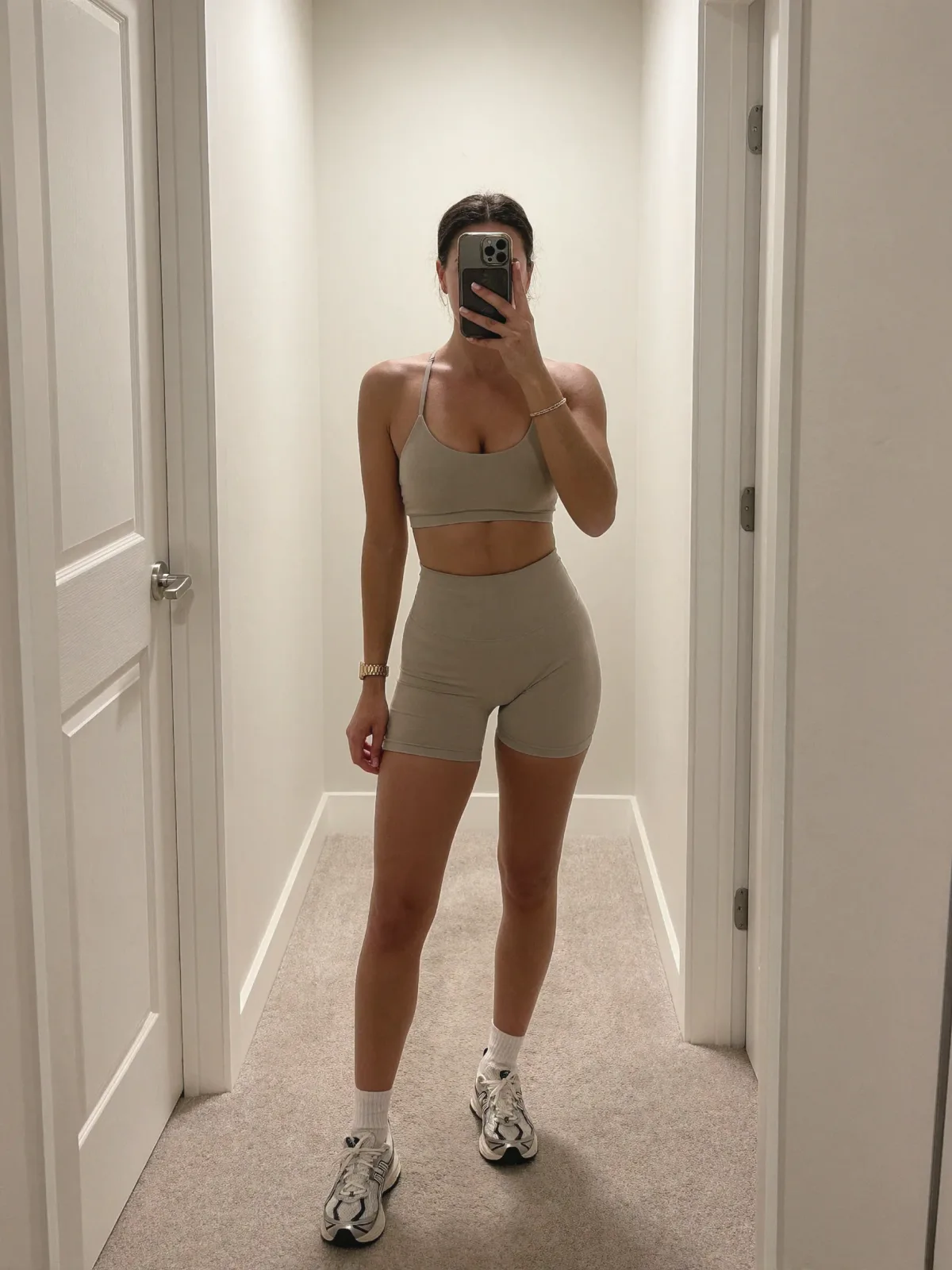 AI photo of a woman with dark hair: hallway mirror selfie in a taupe gym set, made with KREA 2