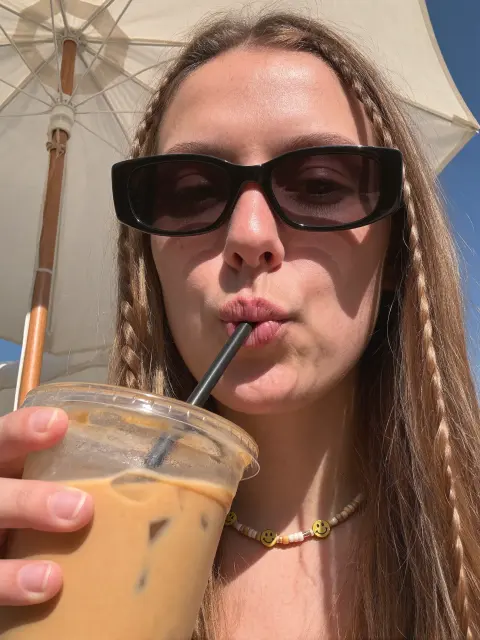 AI photo of a woman with long light-brown hair: iced coffee sip in sunglasses, made with KREA 2
