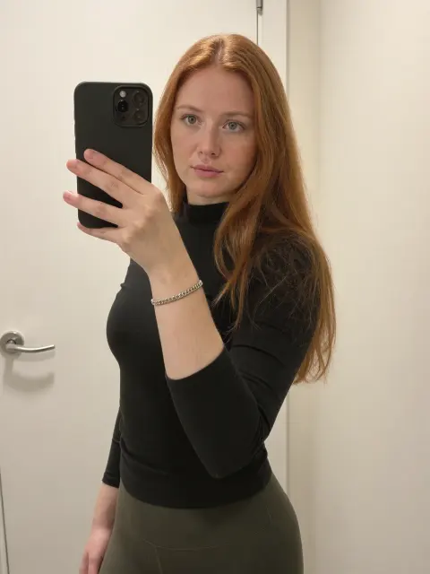 AI photo of a woman with wavy copper-red hair: mirror selfie in a black fitted top, made with KREA 2