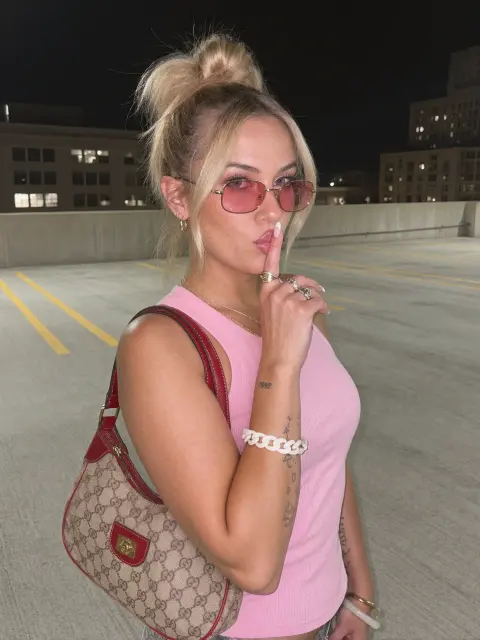 AI photo of a woman with blonde hair: pink top parking garage shush pose, made with KREA 2
