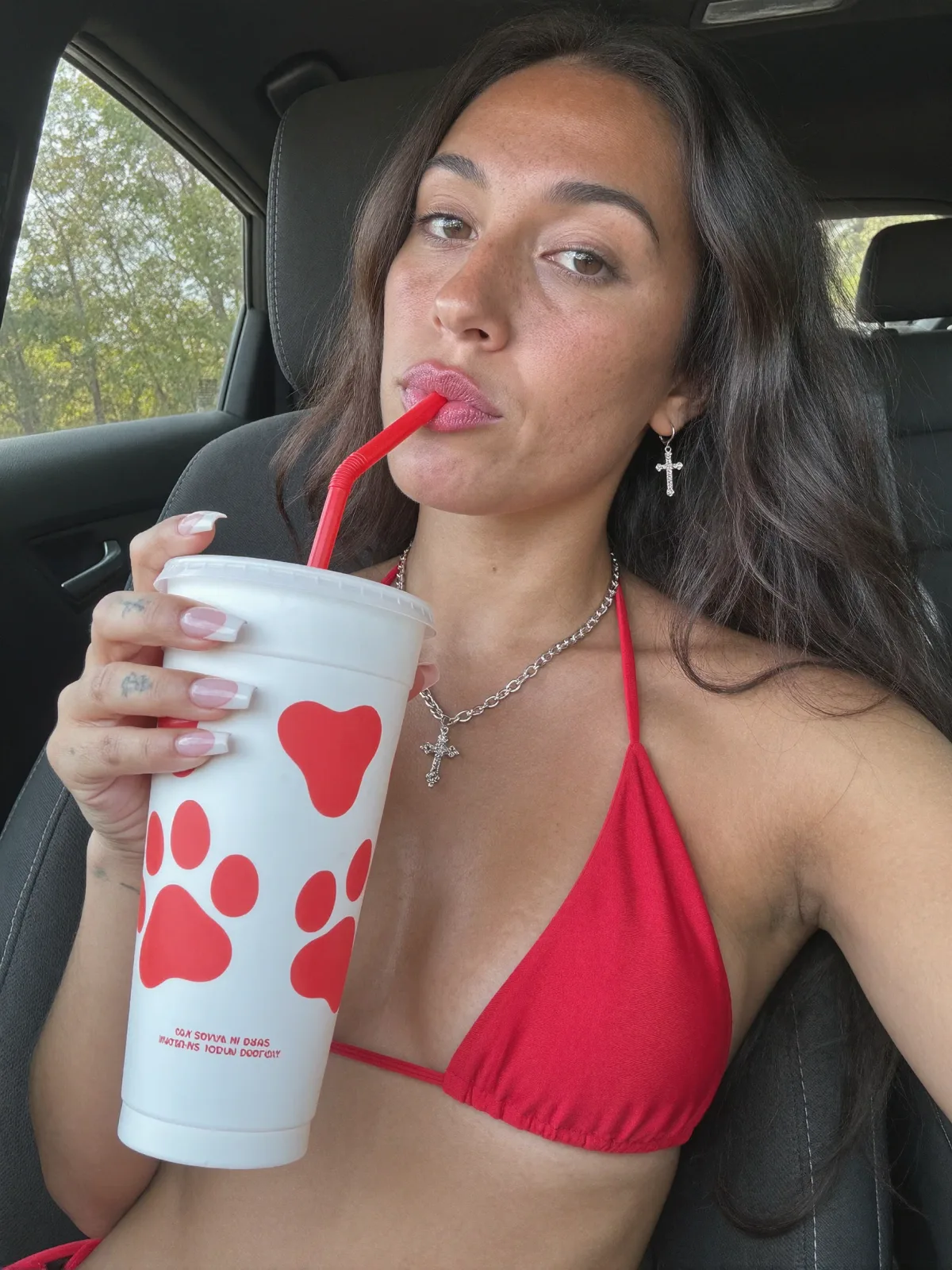 AI photo of a woman with long dark wavy hair: red bikini top with an iced drink in the car, made with KREA 2