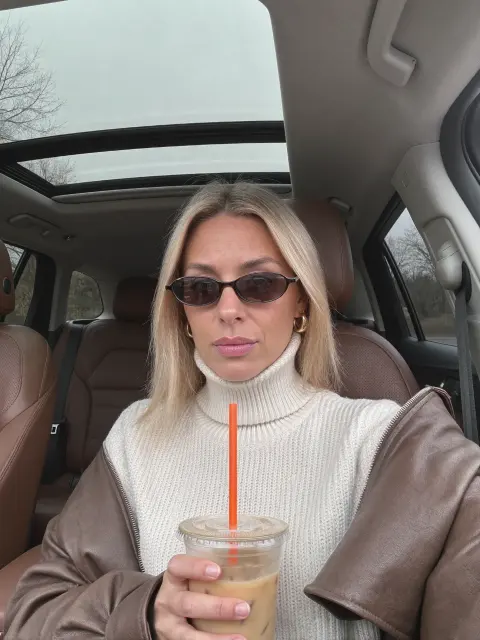 AI photo of a woman with straight shoulder-length blonde hair: turtleneck and iced coffee in the car, made with KREA 2
