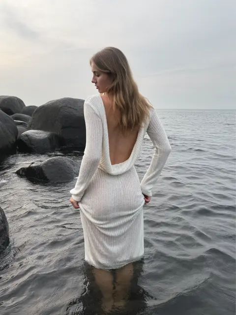 AI photo of a woman with long wavy honey-blonde hair: white knit dress wading into the sea, made with KREA 2