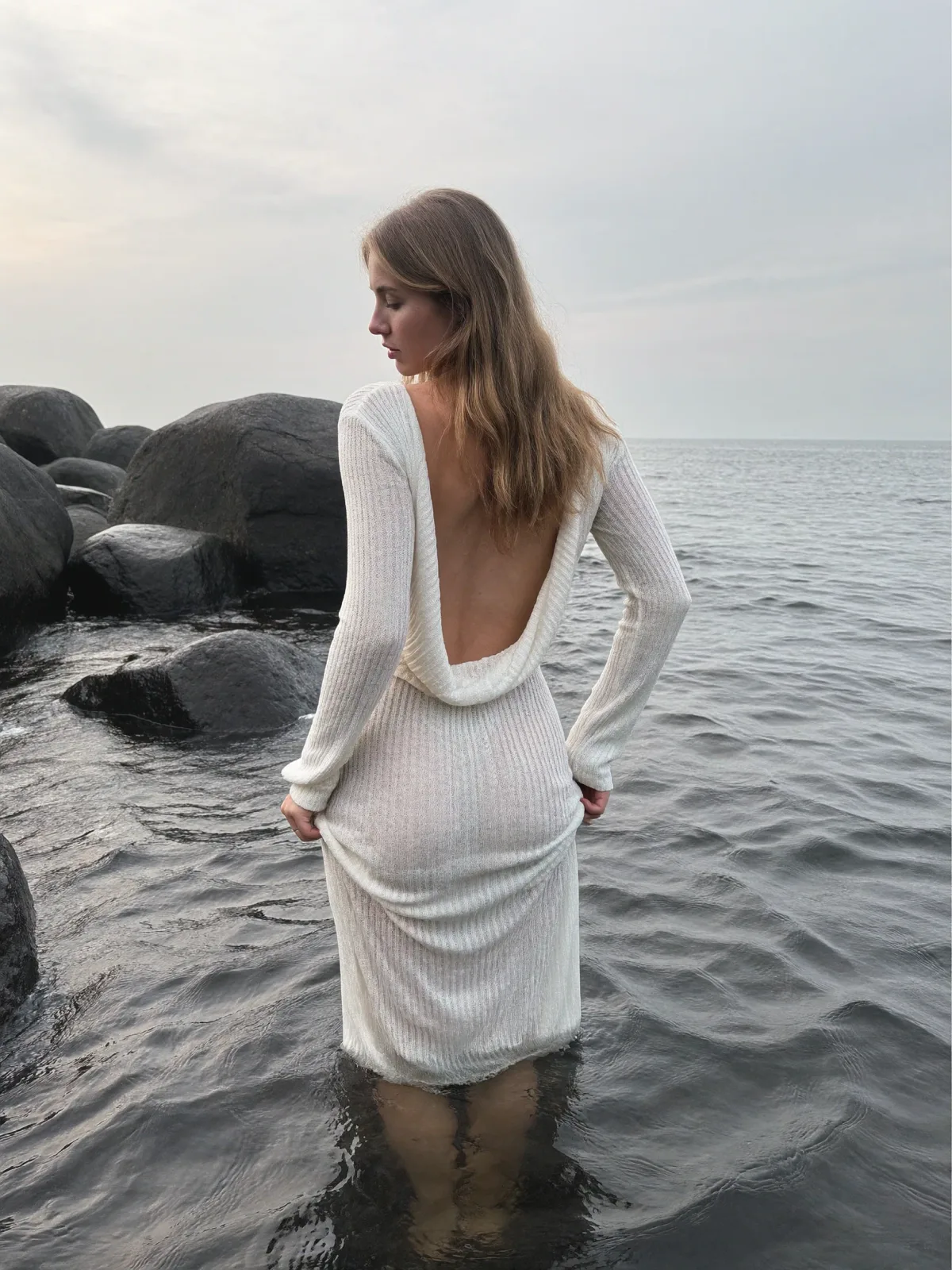 AI photo of a woman with long wavy honey-blonde hair: white knit dress wading into the sea, made with KREA 2